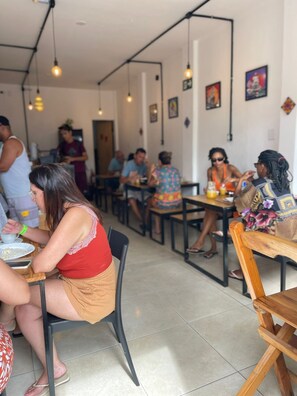 A restaurant with multiple tables and chairs, people dining, and hanging light fixtures. - Grand' Hostel (Sao Cristovao)