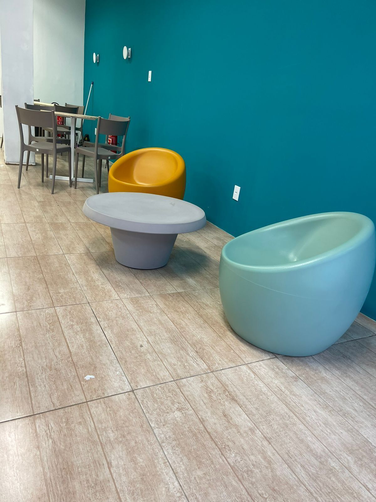 Um interior moderno com paredes verde-água, uma mesa cinzenta e cadeiras coloridas.