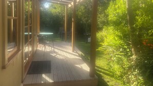 A covered patio with a wooden deck, glass doors, and a table with chairs.