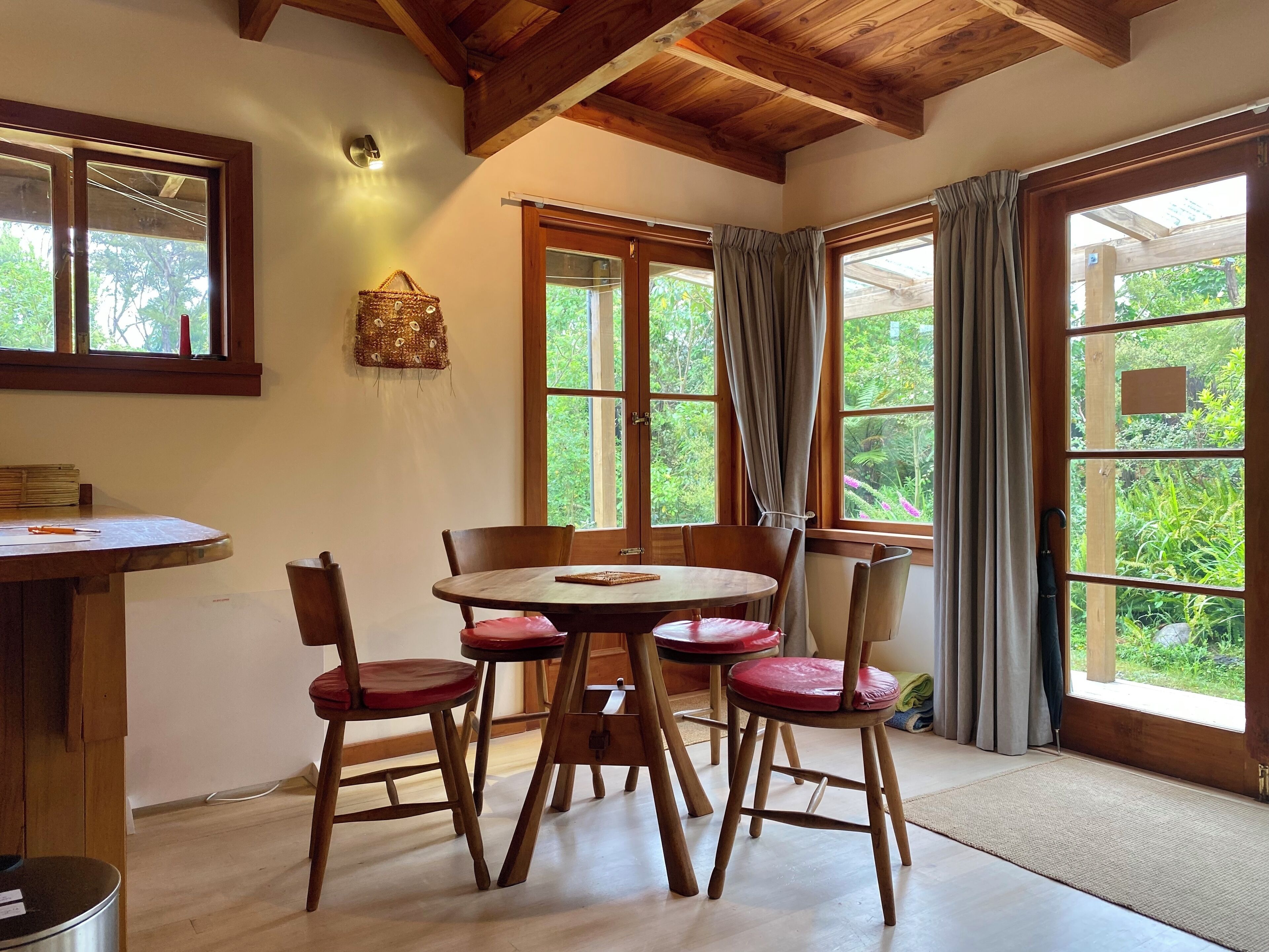 A dining area with a round wooden table, six wooden chairs with red cushions, and a wooden ceiling with exposed beams.