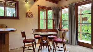A dining area with a round wooden table, six wooden chairs with red cushions, and a wooden ceiling with exposed beams.