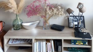 A flat-screen TV mounted on a wall displaying a show. Below the TV, there is a wooden console with a vase of dried flowers, a bowl, and a lamp. - Residential apartment very close to the sea  (Blanes)