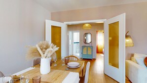A dining area with a table set for two, a vase with dried flowers, and a view into a bathroom through an open door. - Chez Léa + 1 parking (Colmar)