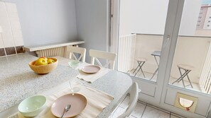 Un balcone con tavolo apparecchiato per consumare i pasti, sedie, una ciotola di frutta e vista su degli edifici.