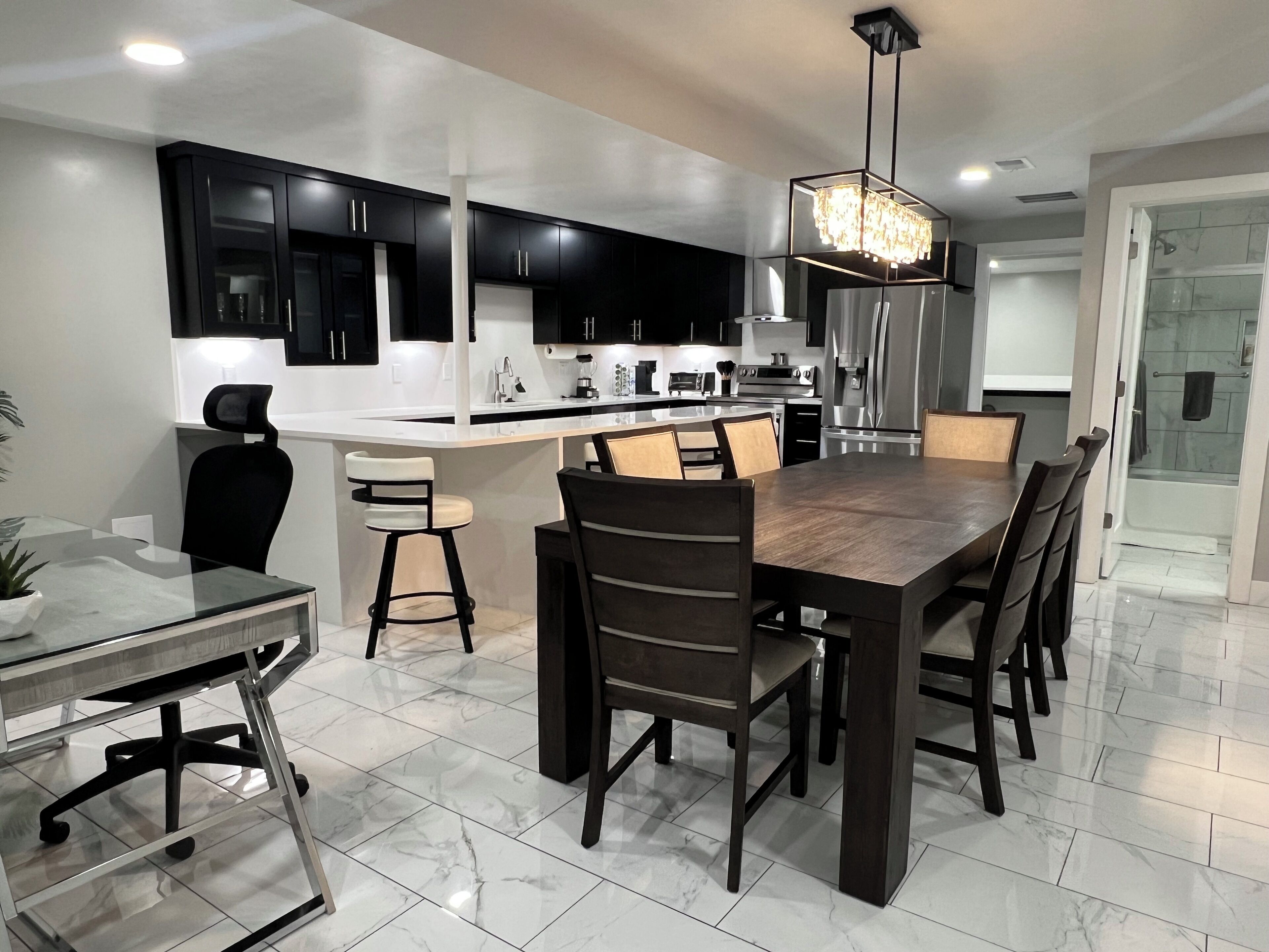 A modern kitchen with black cabinets, a central island, and a dining area with a wooden table and chairs.