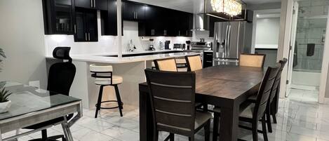 A modern kitchen with black cabinets, a central island, and a dining area with a wooden table and chairs.
