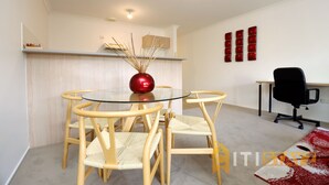A modern room with a glass-top table surrounded by four wooden chairs, a red spherical vase, a red wall decoration, and a black office chair.