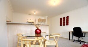 Une pièce moderne avec une table à plateau en verre entourée de quatre chaises en bois, un vase sphérique rouge, un élément décoratif rouge sur le mur et un fauteuil de bureau noir.