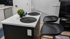 A modern kitchen with a central island, a black chair, and a TV in the background. - President's Choice: Lofty Guest Suite Near Airport  (Edmonton)