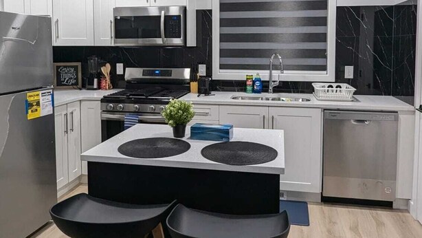 A modern kitchen with white cabinets, a black countertop, a built-in oven, a microwave, and a large window with black marble backsplash. - President's Choice: Lofty Guest Suite Near Airport  (Edmonton)