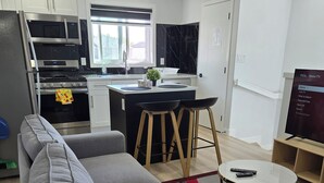 A modern kitchen with a central island, a grey sofa, a small round table, and a TV in the corner. - President's Choice: Lofty Guest Suite Near Airport  (Edmonton)