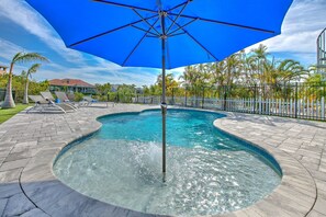 A swimming pool with a blue umbrella, surrounded by a brick patio and palm trees.