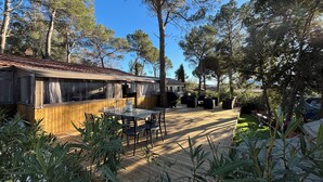 A wooden deck with outdoor furniture, a covered dining area, and surrounding trees.