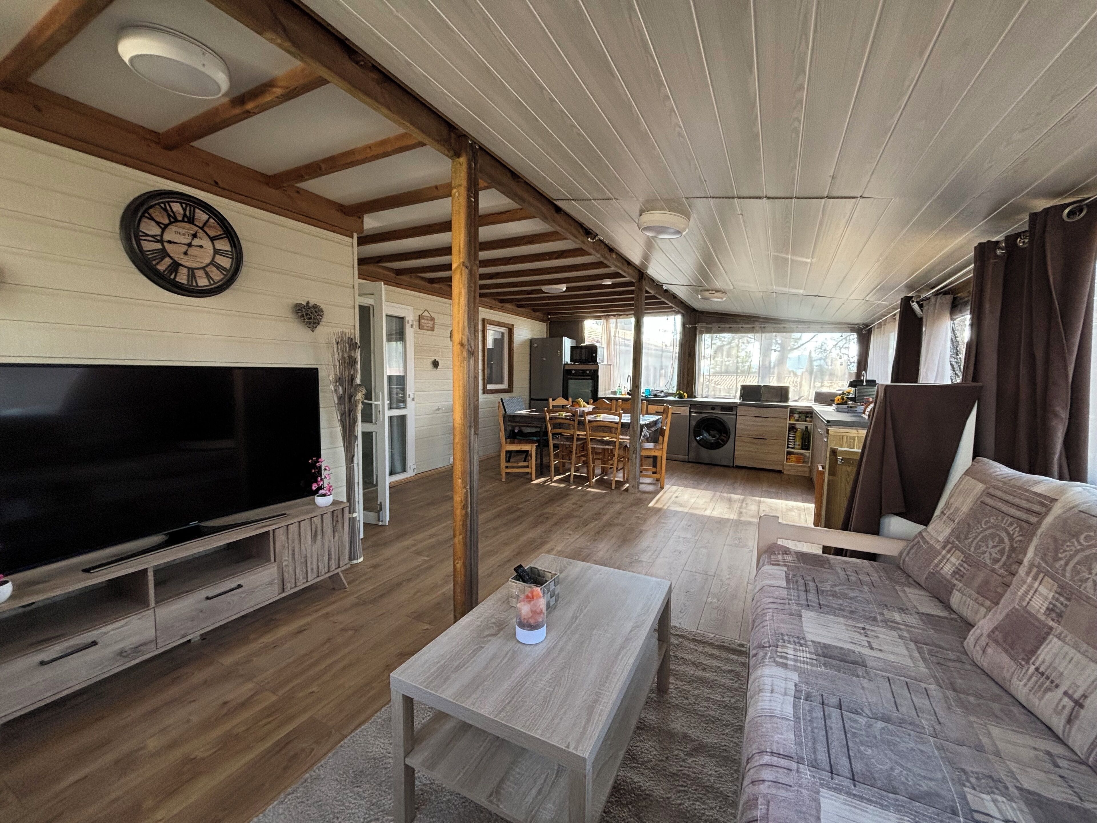 A cozy living room with a flat-screen TV, wooden furniture, and a dining area with a table and chairs.