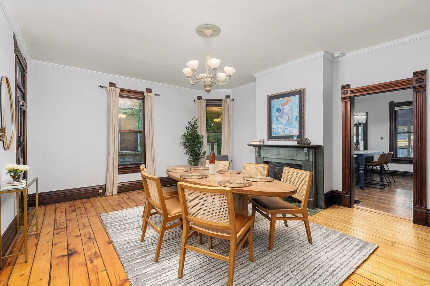 Une salle à manger avec une table ronde en bois, six chaises, un lustre et une cheminée.