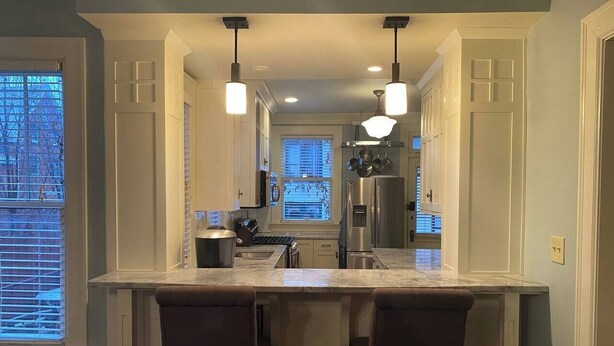 A modern kitchen with a central island, pendant lighting, and a view into the dining area. - The Goodale Park Flat (Columbus)