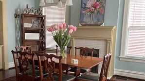 A dining room with a wooden table and chairs, a vase of pink tulips, a bookshelf, and a painting on the wall. - The Goodale Park Flat (Columbus)