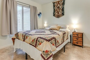Et soveværelse med en stor seng, to sengeborde med lamper, et trænatbord og et vindue med gardiner.
