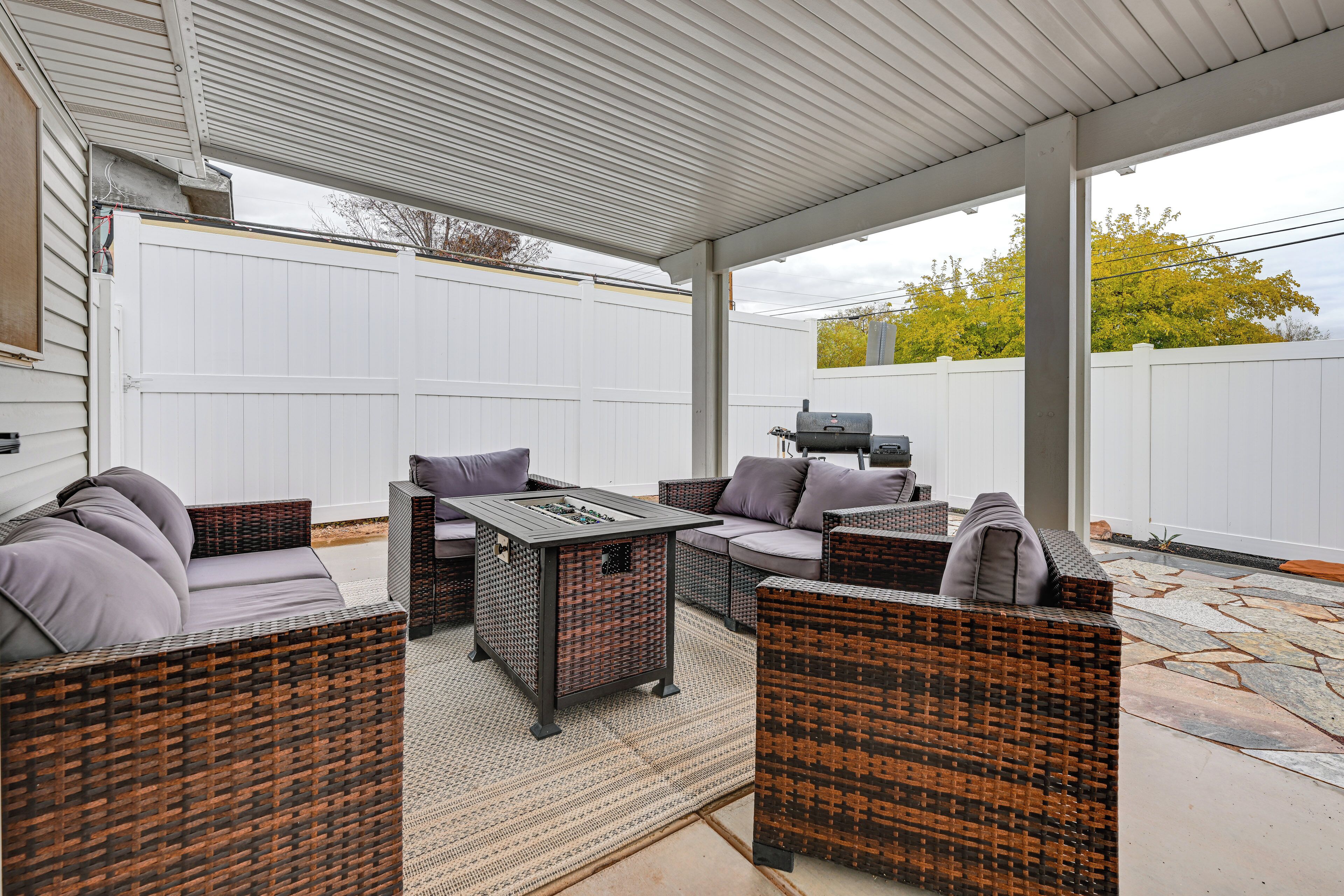 Une terrasse extérieure aménagée avec des meubles en osier, une table à plateau en verre et un barbecue.