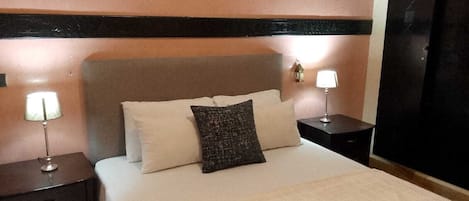 A hotel room with a bed, two bedside tables, and two wall-mounted lamps.