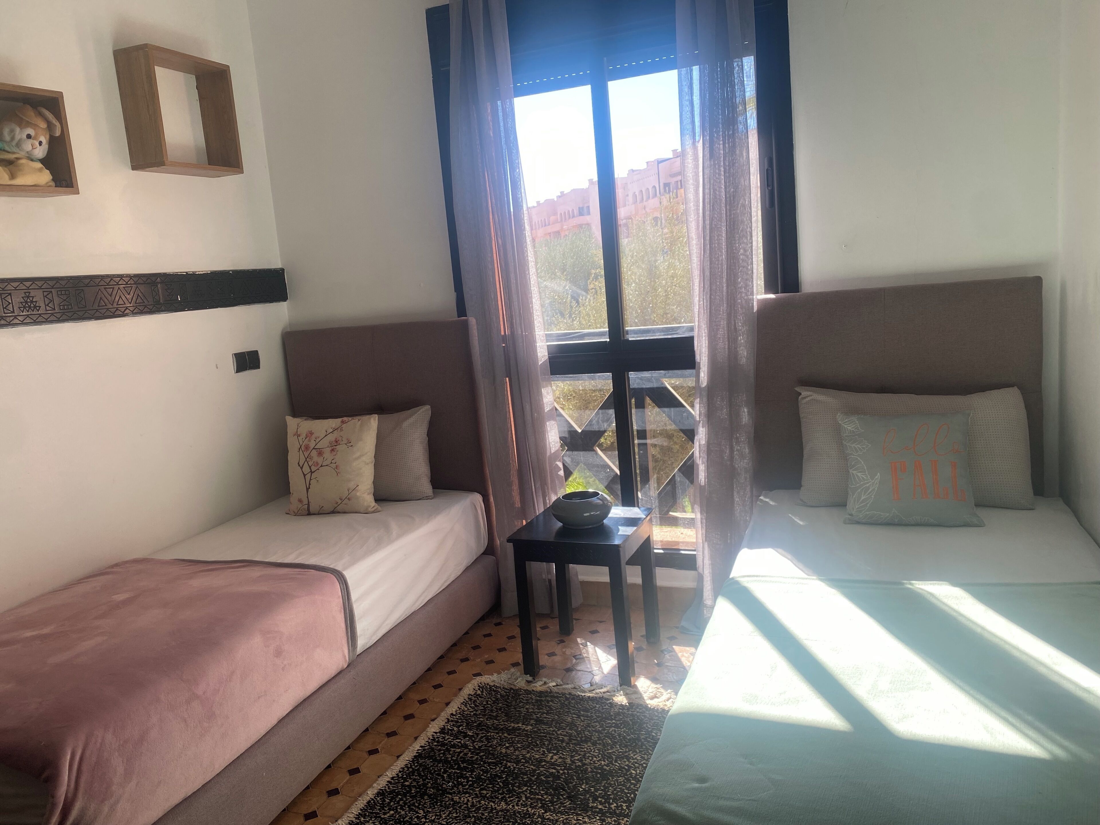 A room with two beds, a small table, and a window with curtains.