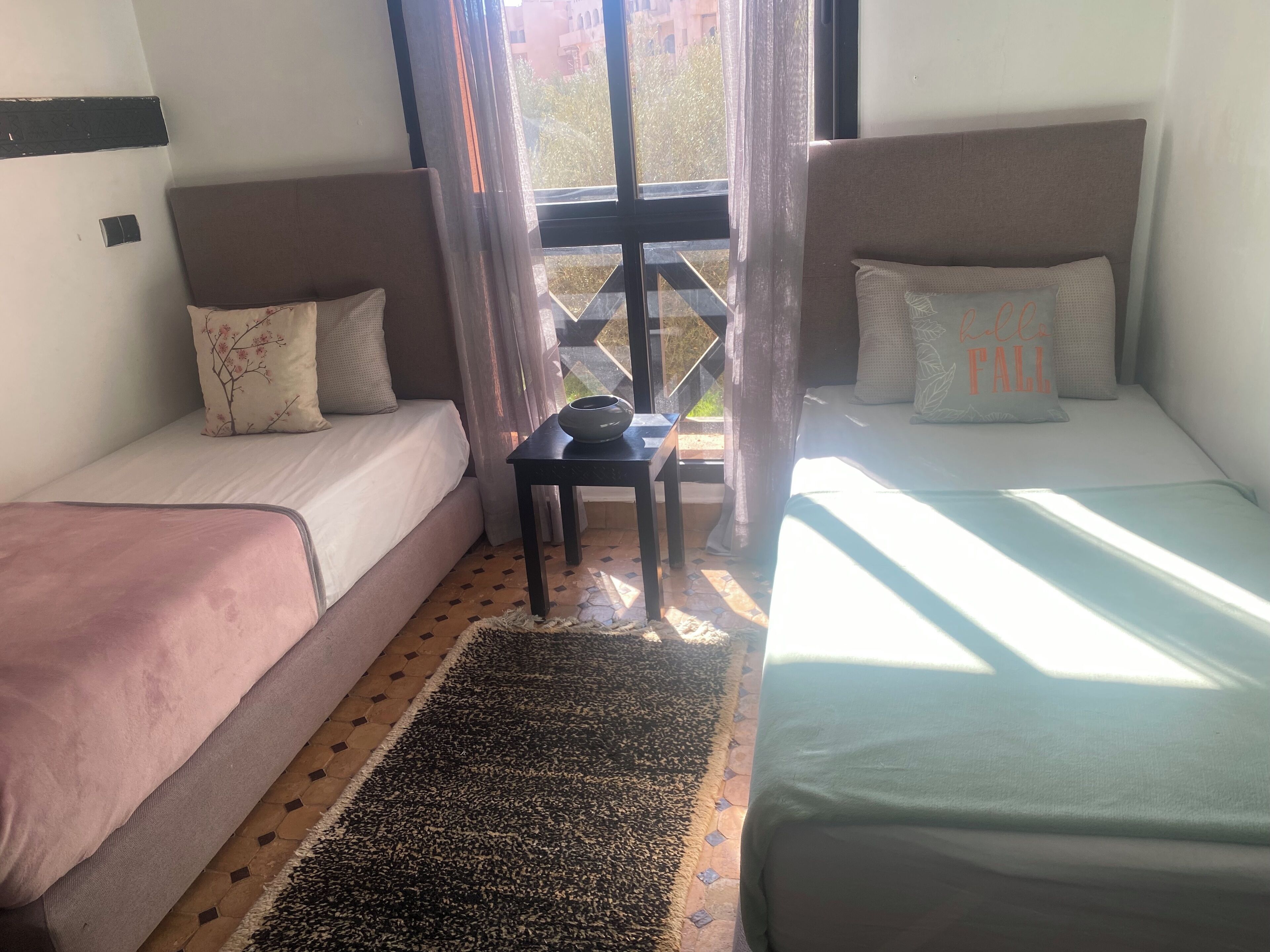 A room with two single beds, a small table, and a window with curtains.