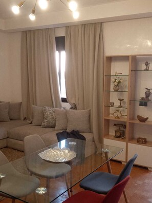 A living room with a sectional sofa, a glass coffee table, and a decorative shelf with various items. - Appartement confortable  (Marrakech)