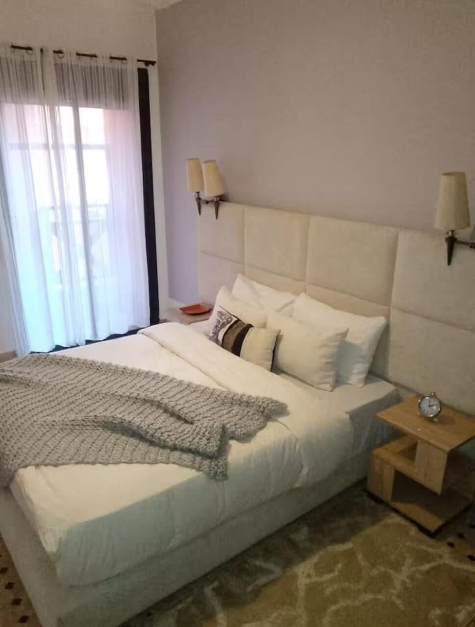 Ein Hotelzimmer mit einem großen Bett, einem Nachttisch mit Lampe und einem Beistelltisch mit einer Uhr.