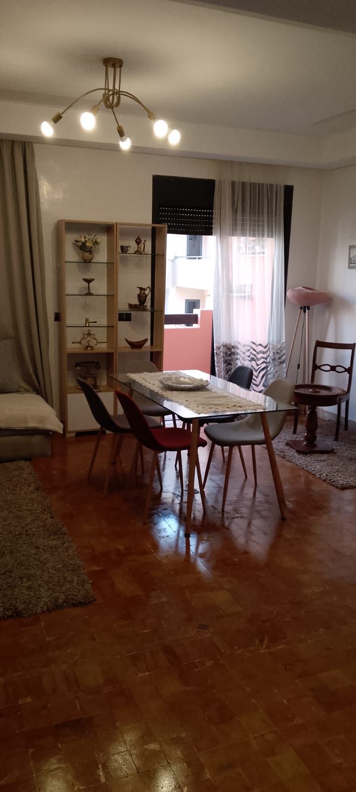 A dining area with a wooden table, chairs, a chandelier, and a bookshelf.