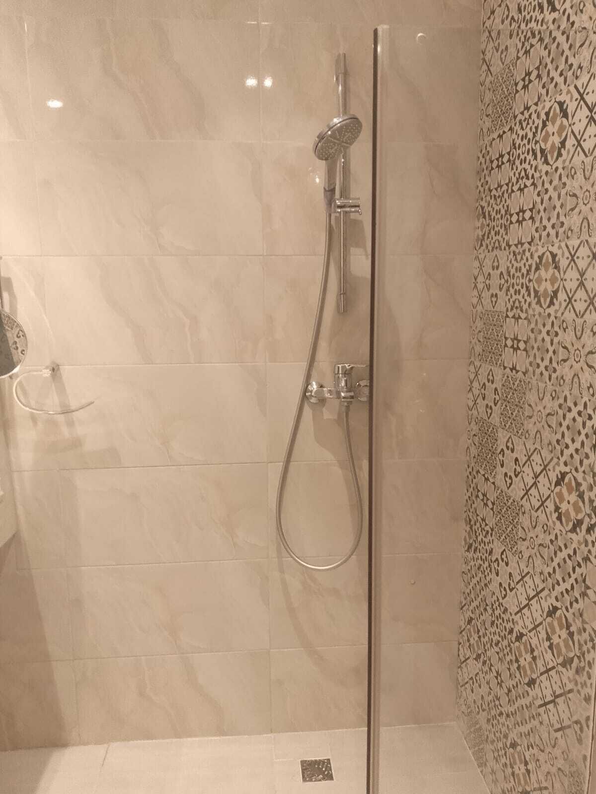 A shower with a handheld showerhead and a wall-mounted faucet.