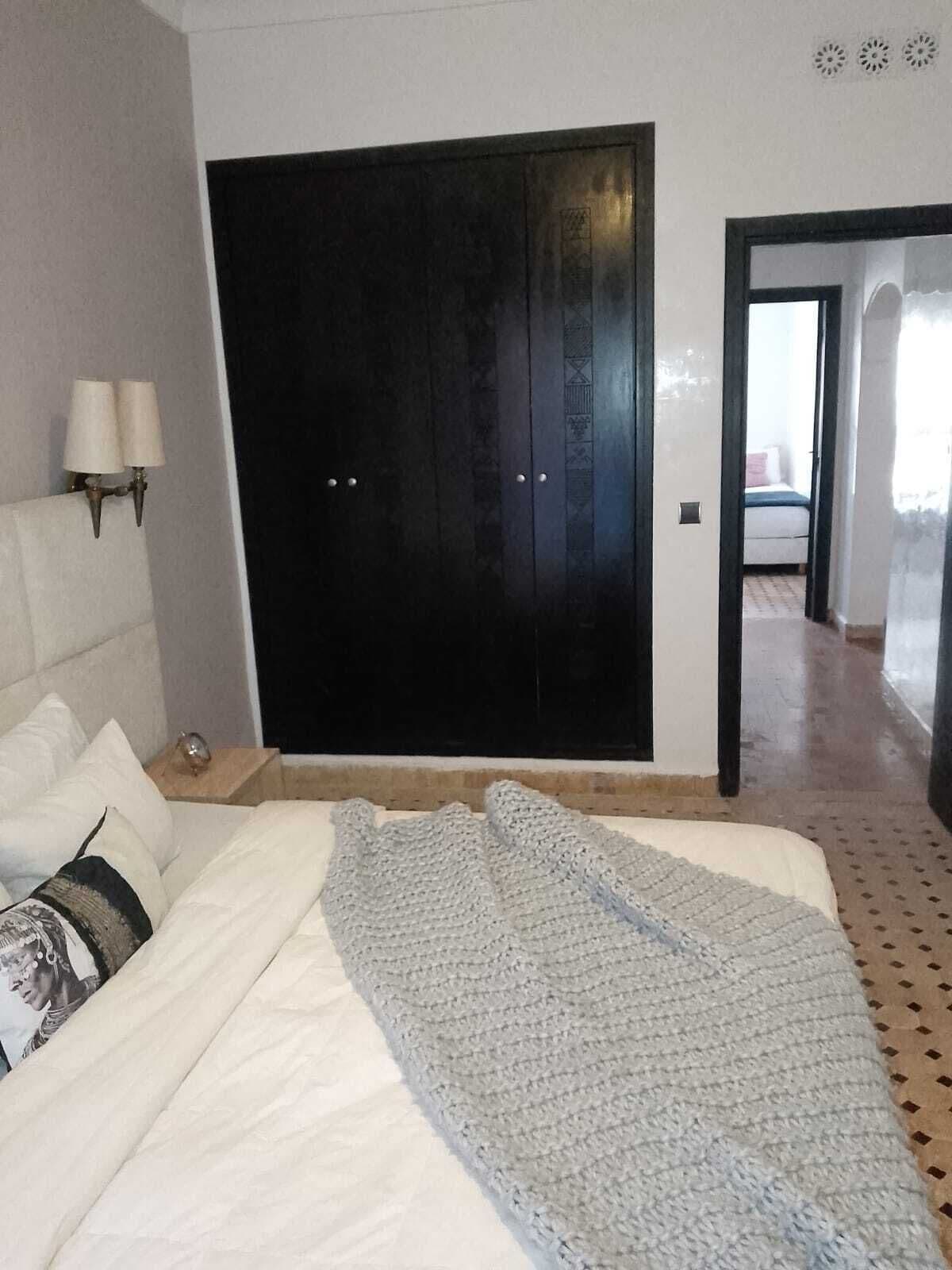 A bedroom with a bed, a dark wardrobe, a nightstand, and a lamp.