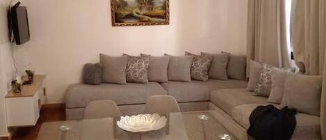 A living room with a glass-top dining table, two chairs, a sofa, and a painting on the wall.