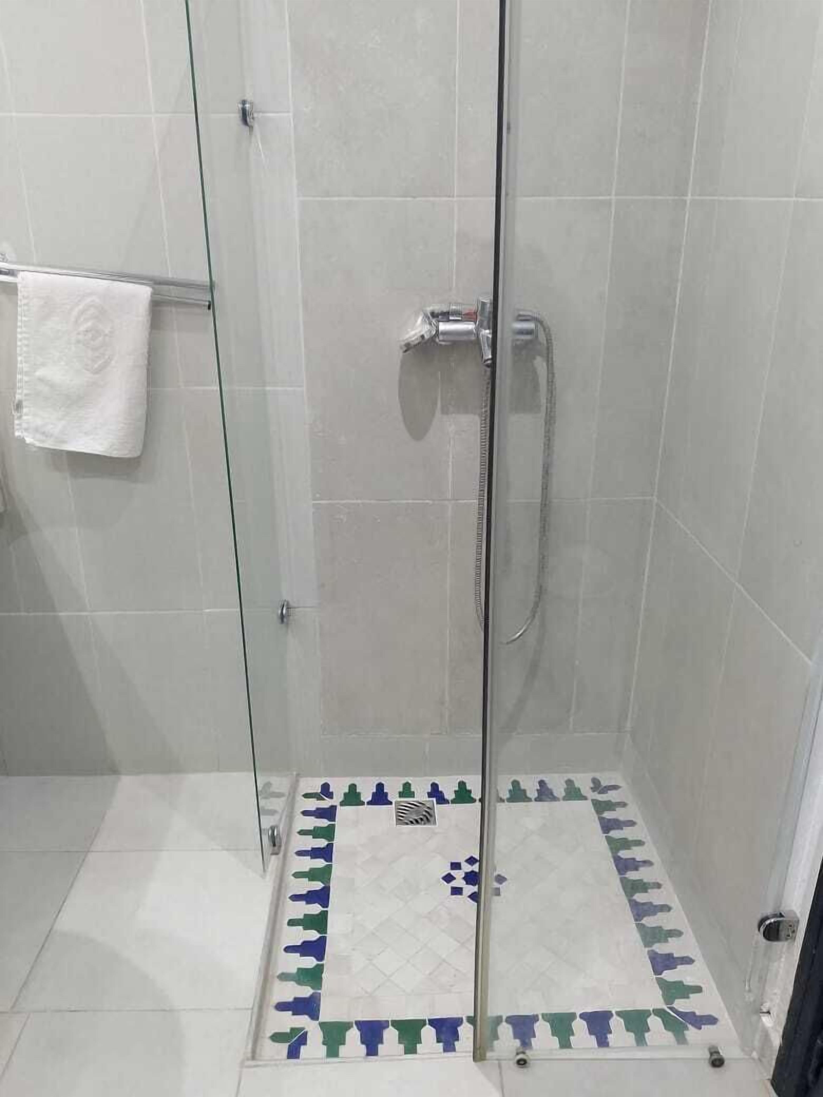 Una ducha con paredes de vidrio y suelo de baldosas con un diseño geométrico.