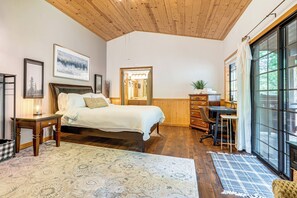 A bedroom with a bed, wooden desk, and large windows. - Fire Pit, Gazebo & Grill: Family Cabin in Arnold! (Arnold)