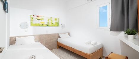 A modern hotel room with two single beds, a wooden bench, a small table, a potted plant, and a window with curtains.
