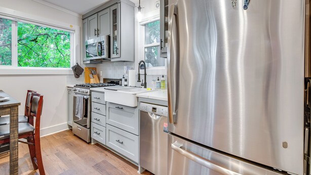 Una cocina moderna con electrodomésticos de acero inoxidable, armarios grises y una ventana con vista a zonas verdes.