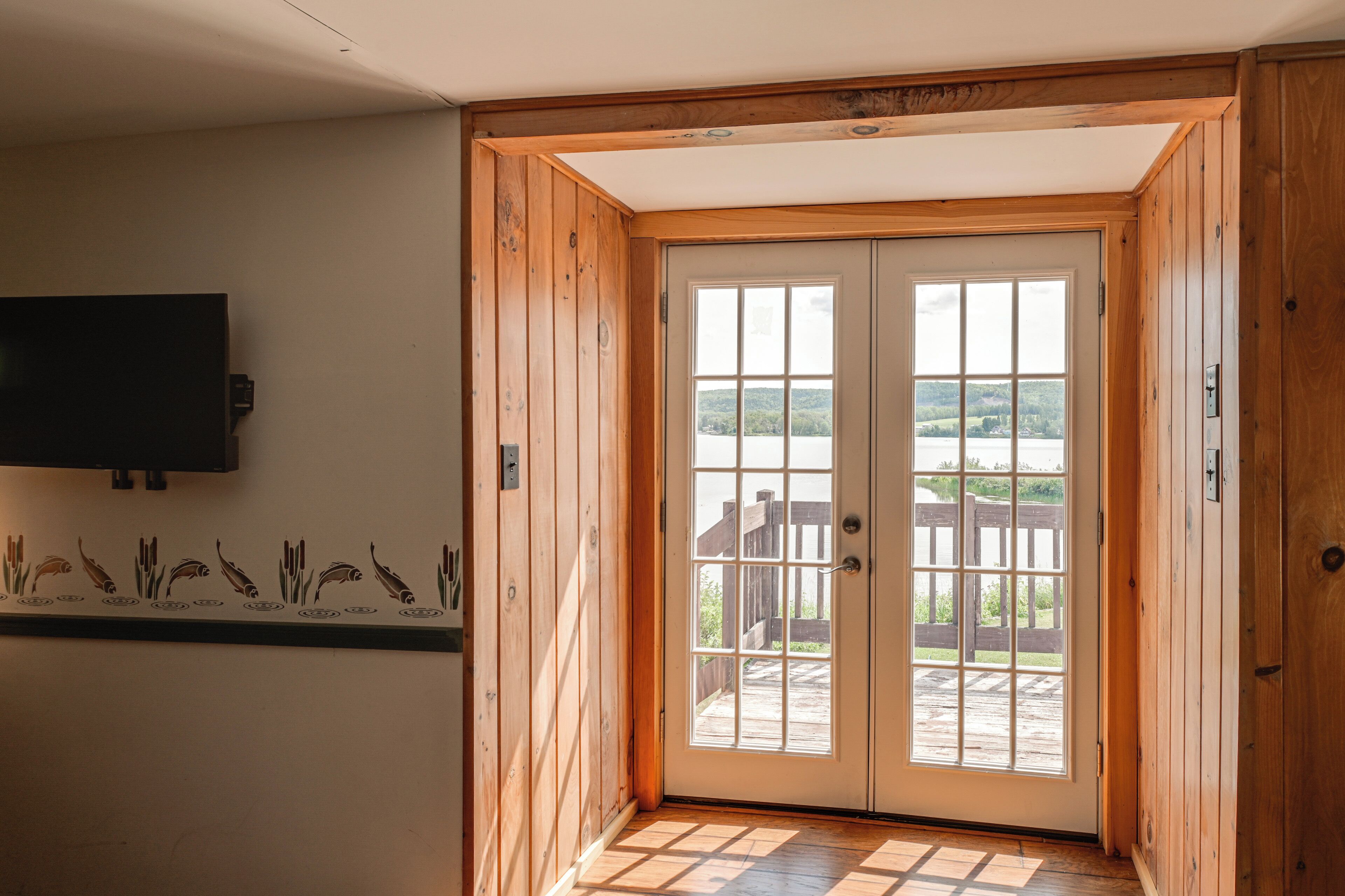 Puerta de madera que da a vistas de un lago y a una terraza de madera.