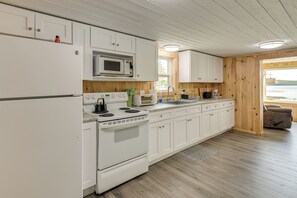 A compact kitchen with white cabinetry, a microwave, a stove, and a sink.