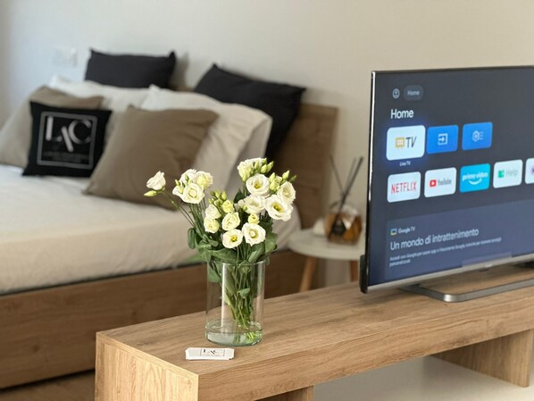 A bedroom with a bed, a TV on a wooden stand, and a vase with flowers on a bedside table.