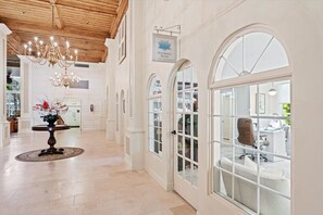 Um corredor amplo com um candelabro, uma mesa redonda com flores e janelas em arco.