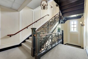Uma escadaria imponente com grades de metal ricamente decoradas e um corrimão de madeira, conduzindo a um andar superior.