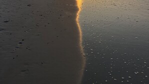 En strand med solnedgang, bygninger i baggrunden og fodspor i sandet.