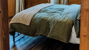 Una habitación de madera con una cama, una araña y un ventanal.