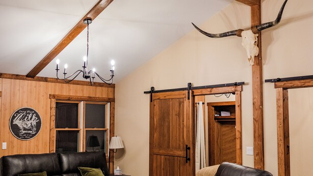 Una habitación con vigas de madera, un sofá de cuero negro, un sillón de cuero y un cráneo de vaca en la pared.