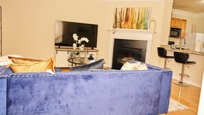 A living room with a blue sofa, a flat-screen TV, a fireplace, and a kitchen area in the background. - Charming 3-bedroom townhome in Duluth  (Duluth)