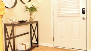 A room with a wooden floor, a white door with blinds, a console table with a vase of flowers, and two wall mirrors. - Charming 3-bedroom townhome in Duluth  (Duluth)