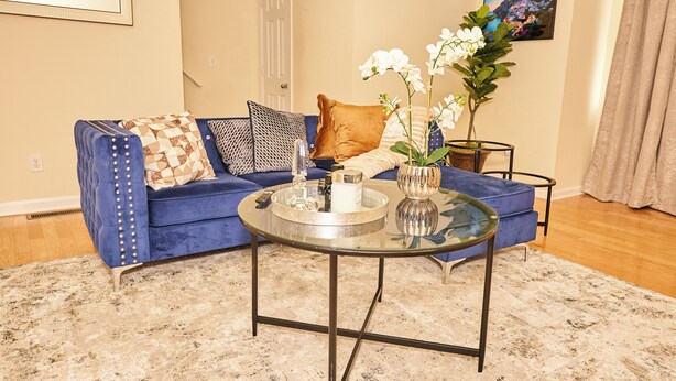 A living room with a blue sofa, patterned pillows, a glass coffee table, and a vase with white flowers. - Charming 3-bedroom townhome in Duluth  (Duluth)