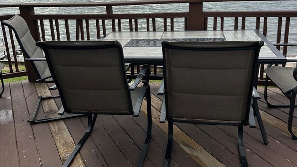 Een houten terras met metalen stoelen en een picknicktafel met uitzicht op een meer.