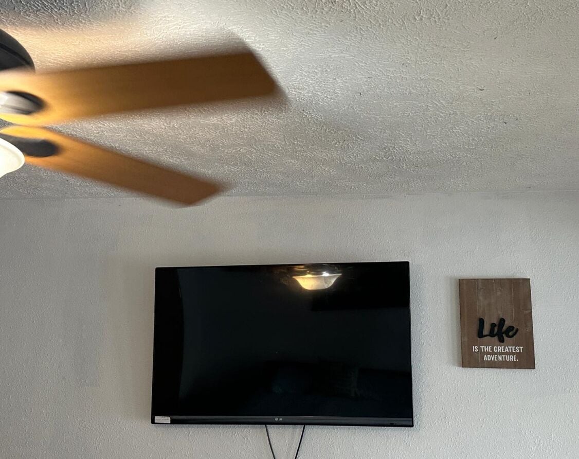 Ein Flachbildfernseher an einer weißen Wand, ein Deckenventilator und ein Schild mit einem motivierenden Spruch.