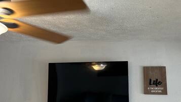 A flat-screen TV mounted on a white wall, a ceiling fan, and a motivational quote sign.
